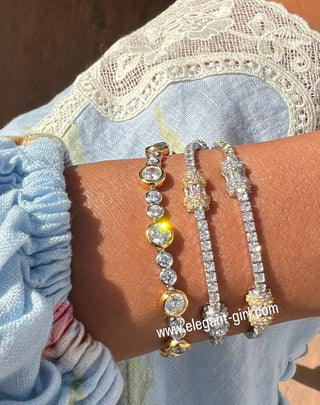 Close-up of a wrist wearing two gold and diamond bracelets with a blurred background.